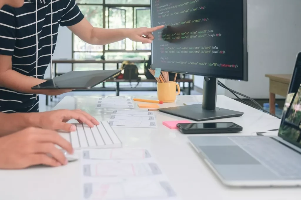 Two developers reviewing HTML form code and page wireframes during a website build